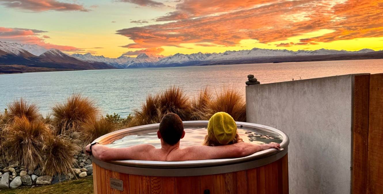 Couple relaxing in the private hot tub at the Lake View Spa Suite overlooking Lake Pūkaki at sunset