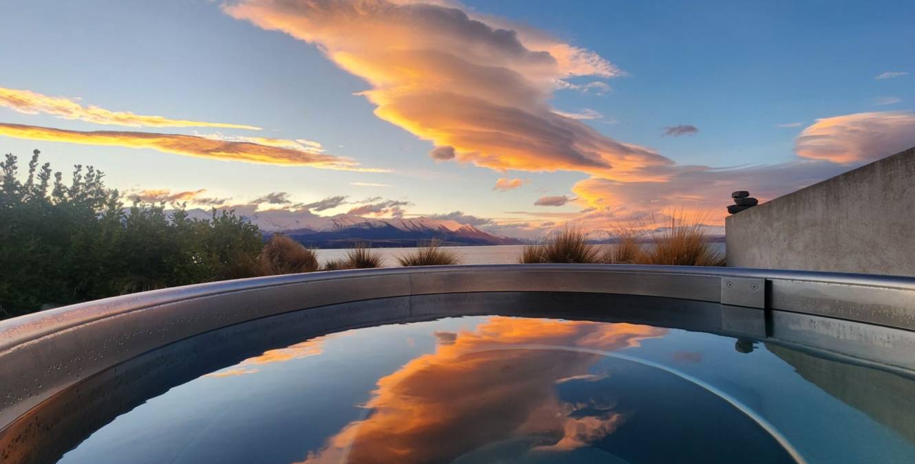 Private hot tub at the Lake View Spa Suite overlooking Lake Pūkaki with colourful sunset reflections across the Southern Alps