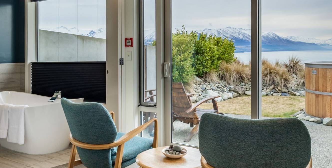Lake View Spa Suite with lounge seating, freestanding bath, private cedar hot tub and views across Lake Pūkaki to Aoraki Mount Cook National Park